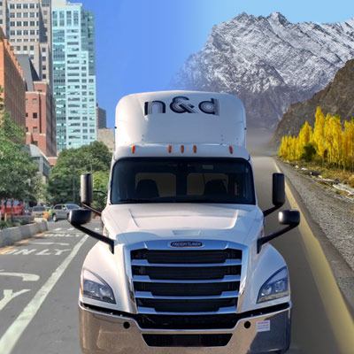 N&D truck driving on road in front of mountains and buildings