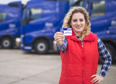 woman showing her cdl drivers license in front of blue trucks