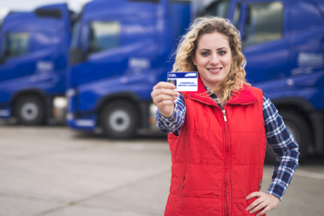 woman showing her cdl drivers license in front of blue trucks