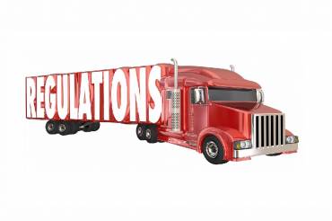 transportation regulations signified by the word regulations on the side of a red 18 wheeler truck