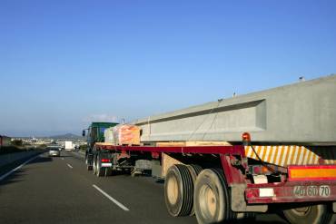 Heavy hauling truck transporting a large concrete beam on a flatbed trailer along a highway.