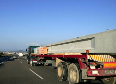 Heavy hauling truck transporting a large concrete beam on a flatbed trailer along a highway.