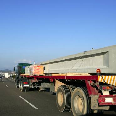 Heavy hauling truck transporting a large concrete beam on a flatbed trailer along a highway.